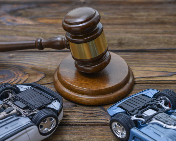 Picture of a wooden judges gavel and two flipped-over toy cars sitting in front of it.